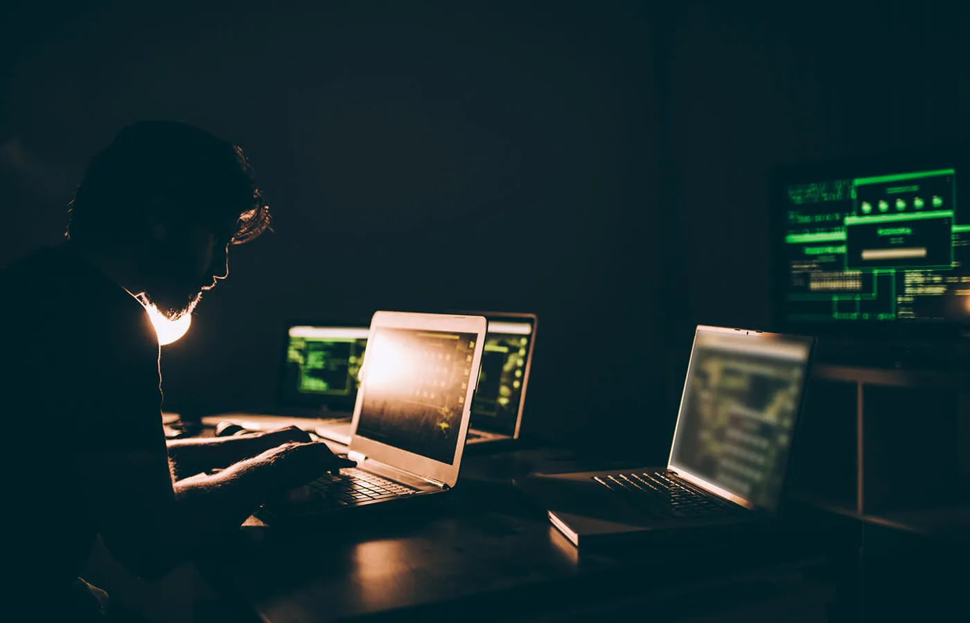 man in dark room surrounded by open laptop screens