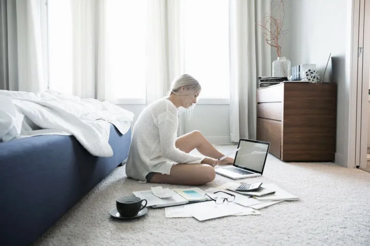 woman sitting on the floor surrounded by papers in front of an open laptop