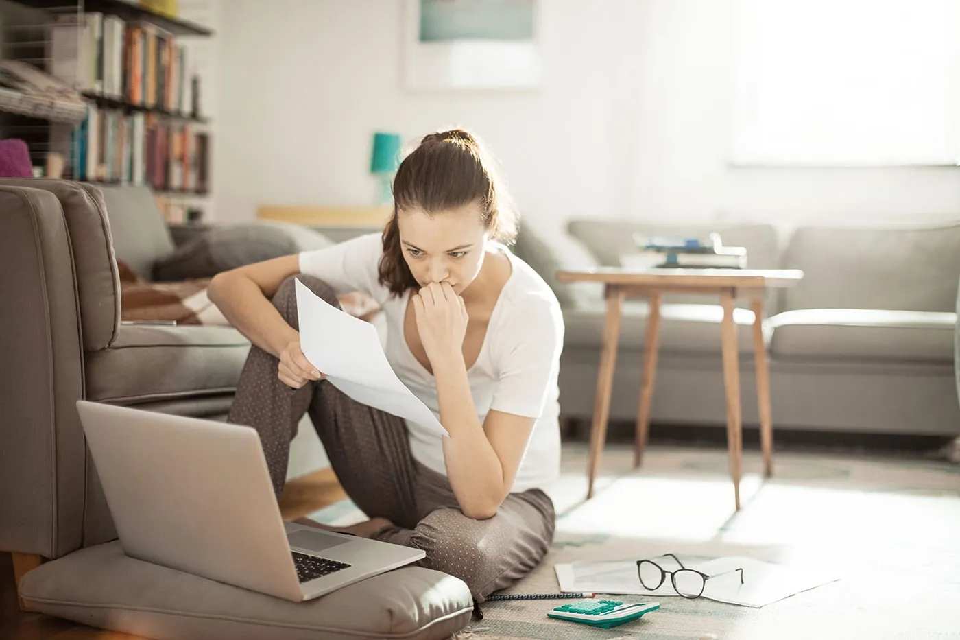 young woman holding a paper and looking at the laptop screen while doing research on bonds