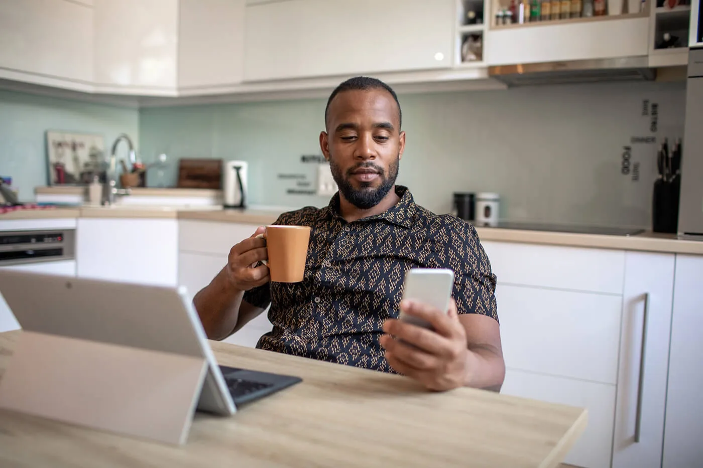 A man Is using his mobile phone and drinking coffee