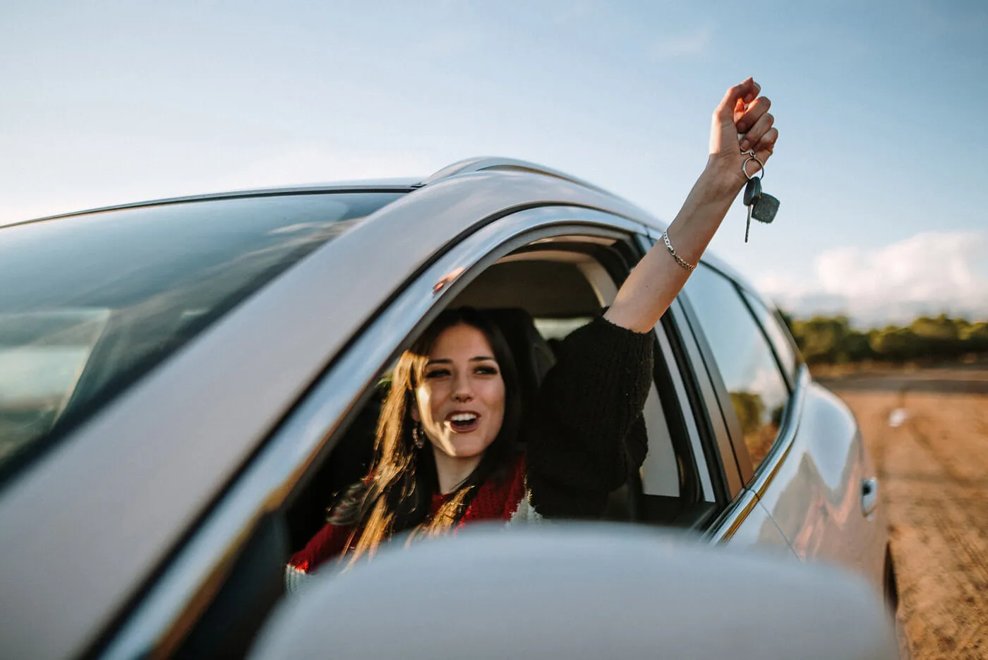 A young woman showing the car keys through the car window