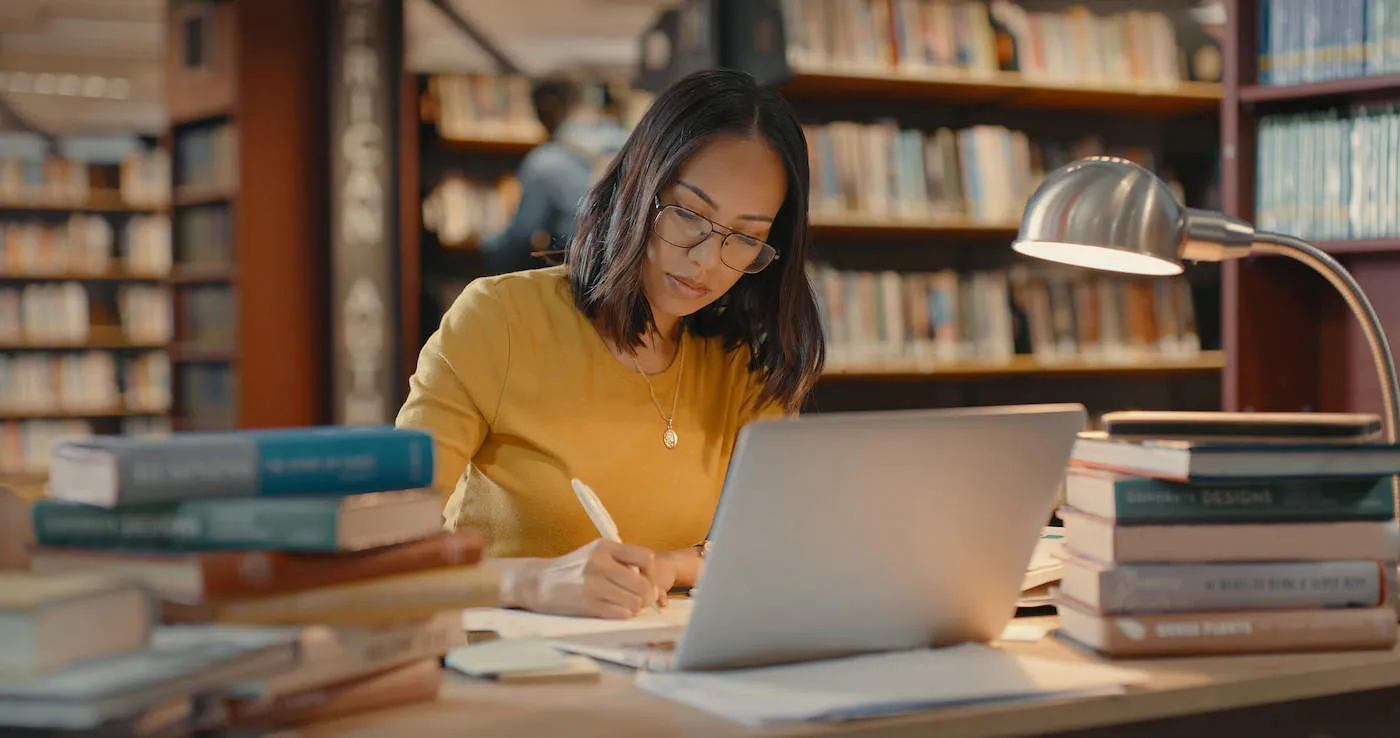 A college student wearing a yellow shirt studies in the library.