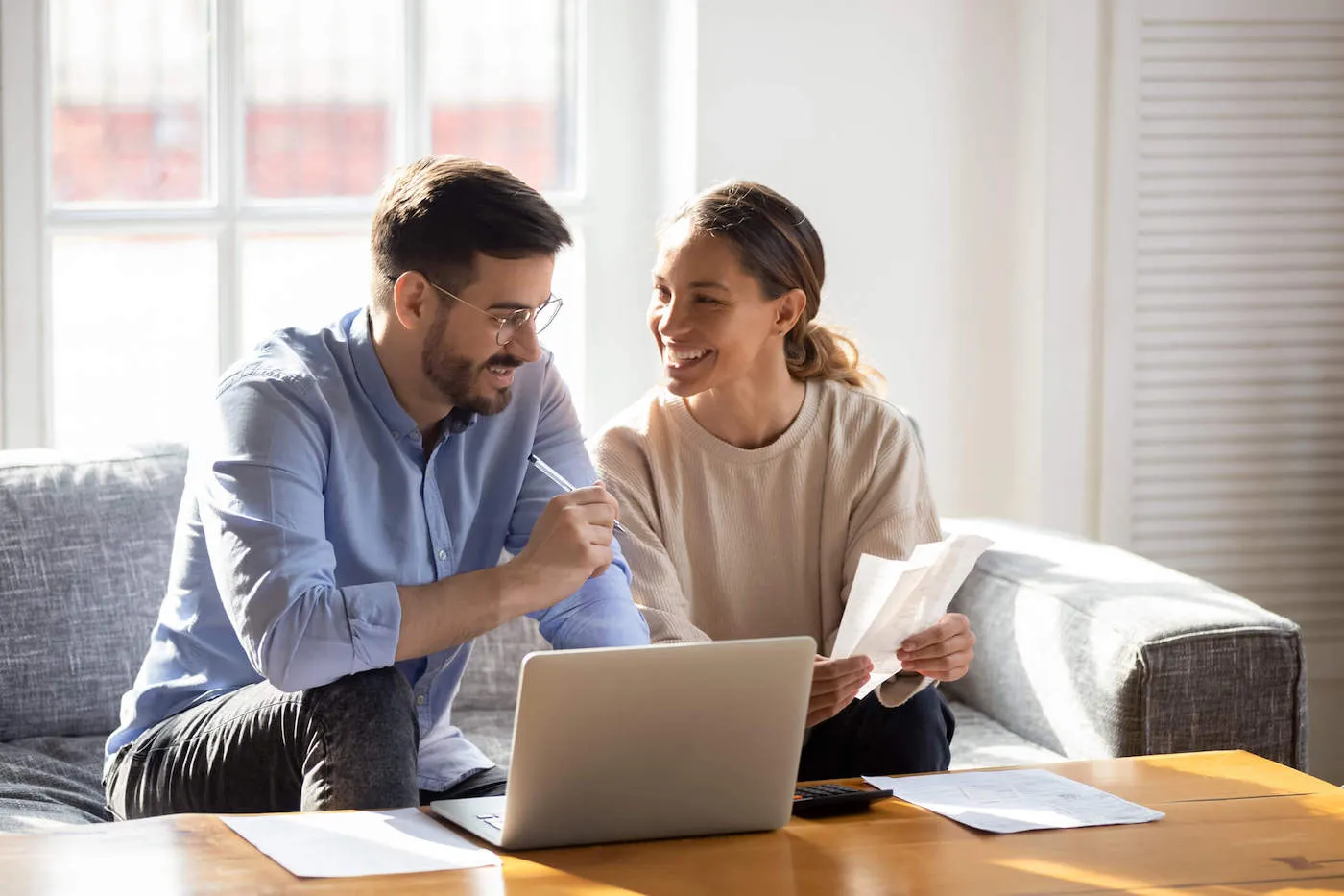 A couple smile together as they look at receipts from the couch.