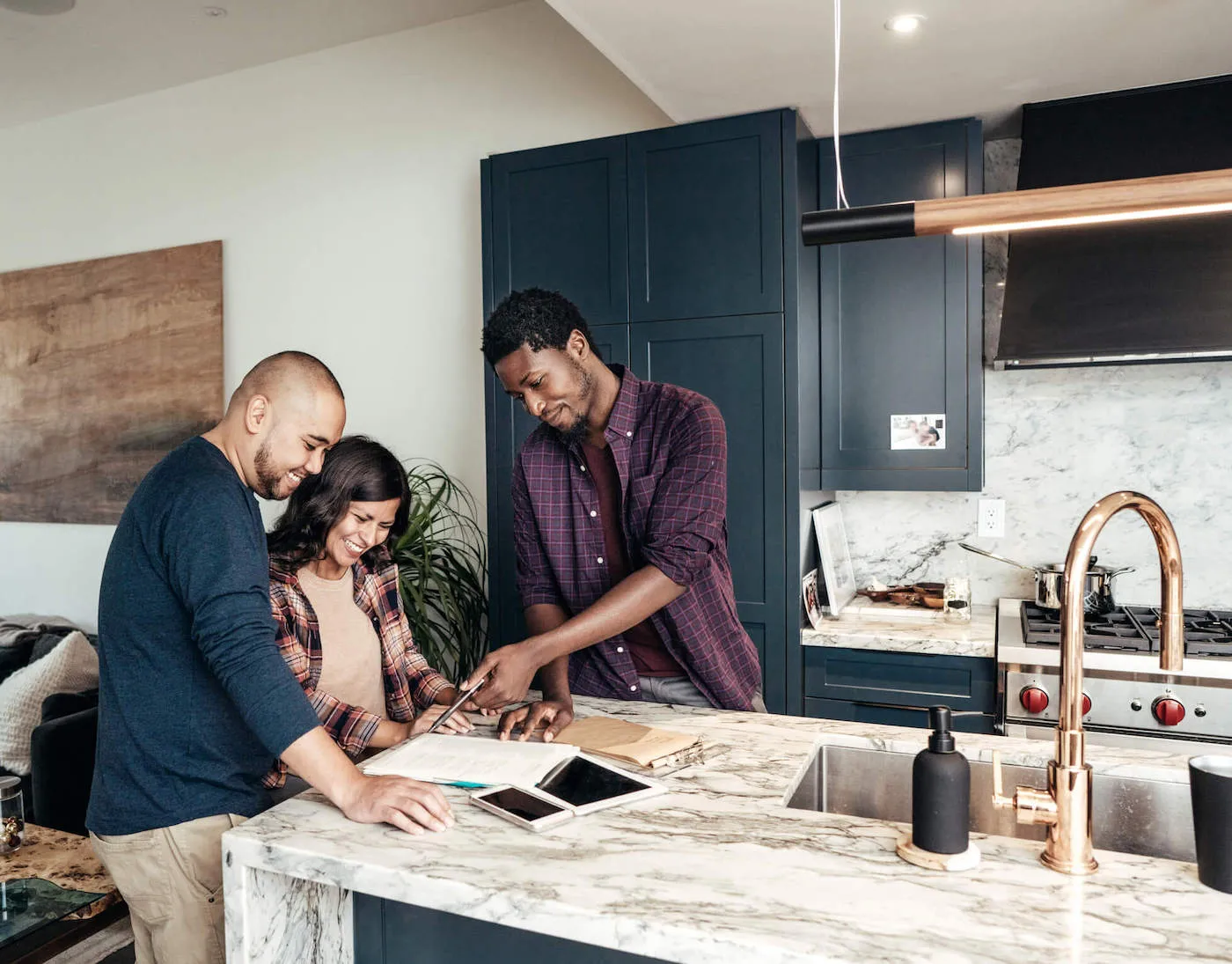 A couple smile together while looking at documents being shown by another person a the kitchen countertop.