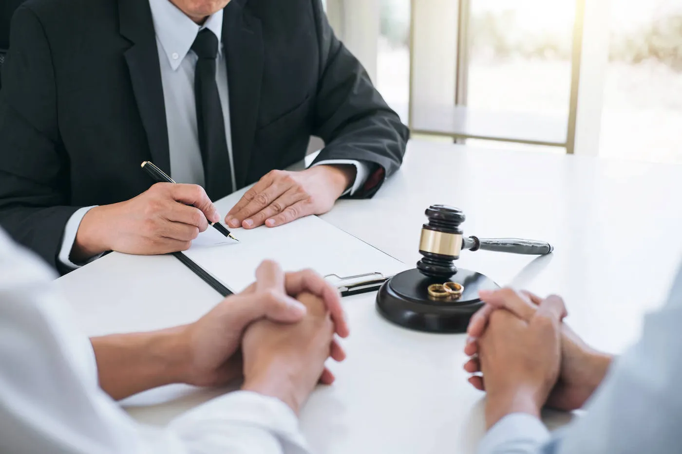 A divorce lawyer wearing a suit writes on a document while meeting with a couple.