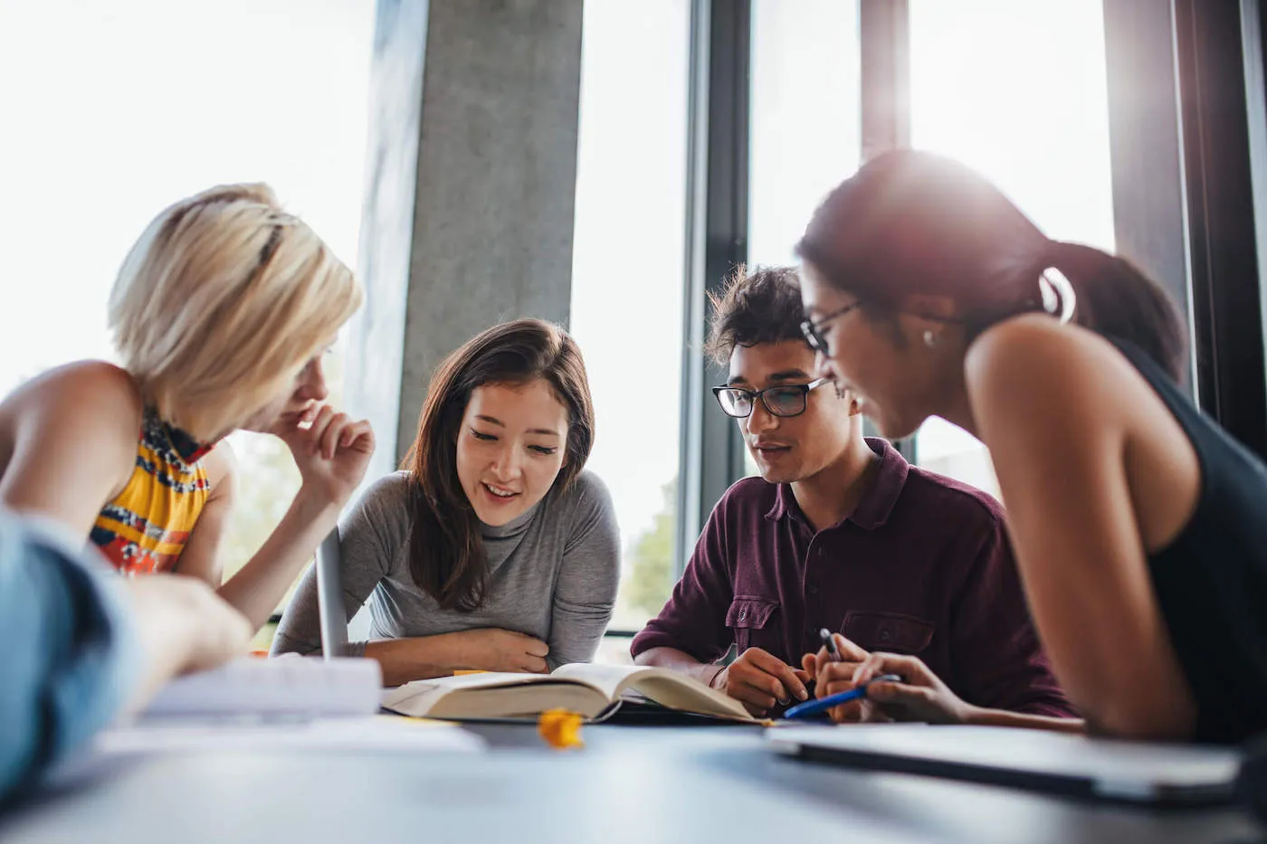 A group of four college students look at a textbook on the table together.