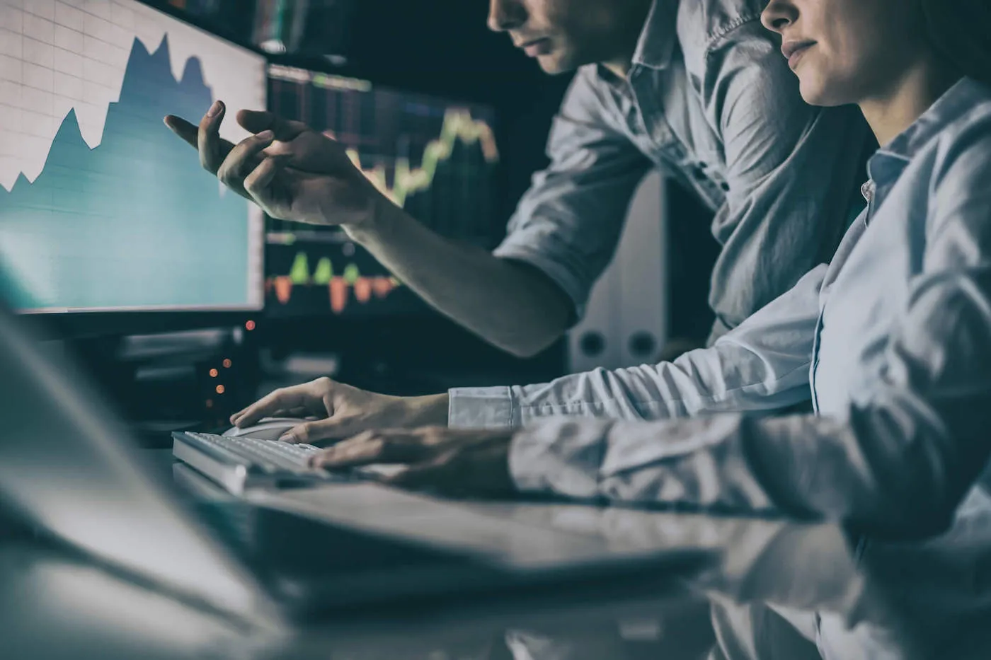 A man and a women wearing light blue shirts are looking at stock investment graphs on the computer.