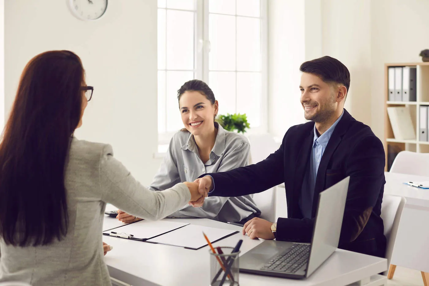 A man shakes hands with a woman across the table while another woman sits next to him.