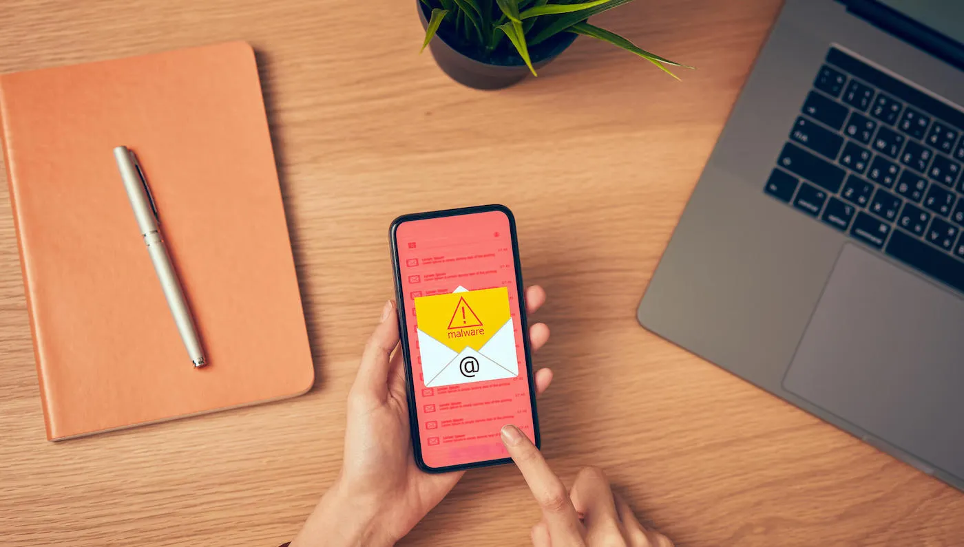 A person holds a phone that has a malware warning email on the screen.