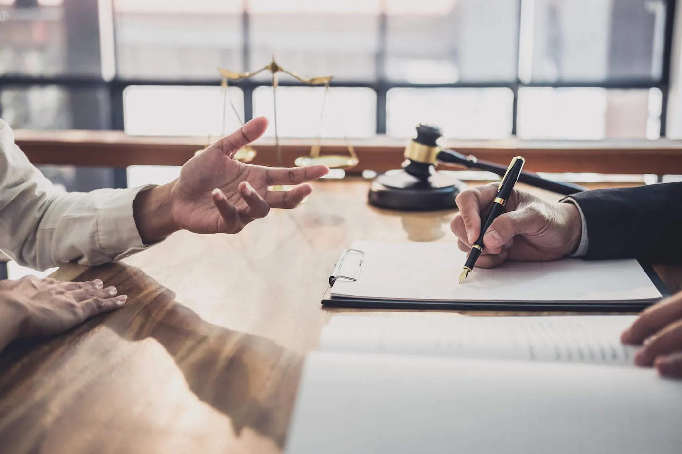 A person across the table talks to another person in a suit while they use a pen to write on a document.