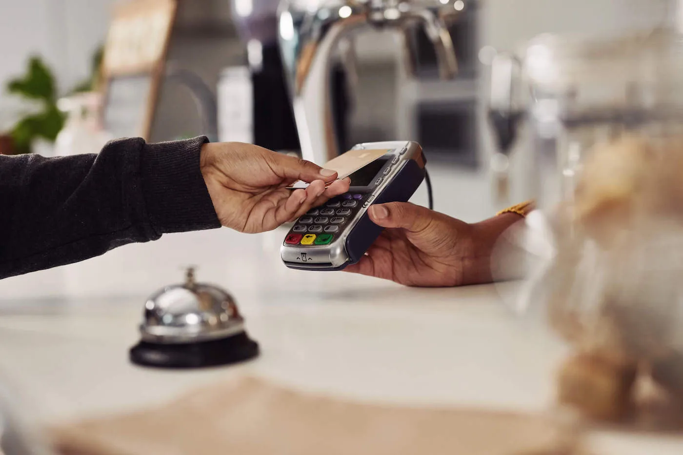 A person taps their credit card on the card reader being held by another person at the bakery shop.