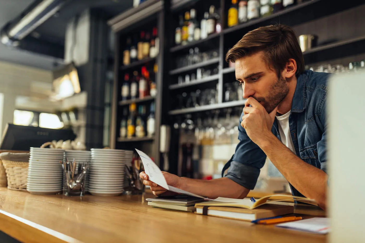 A restaurant owner looks at a document while he has notebooks in front of him.