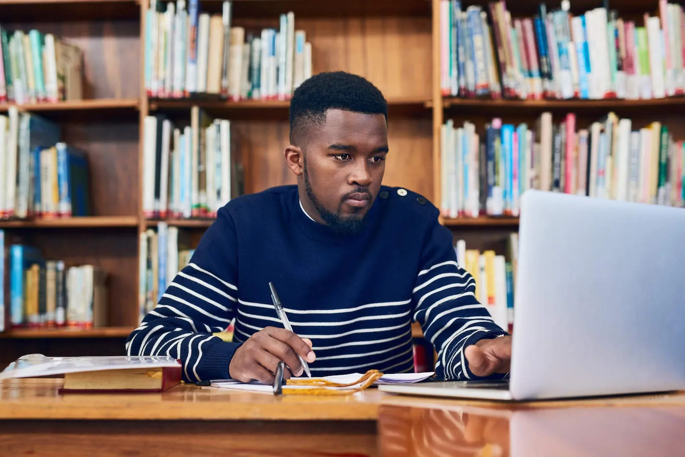 A student writes on his notebook while looking at a computer inside the library.