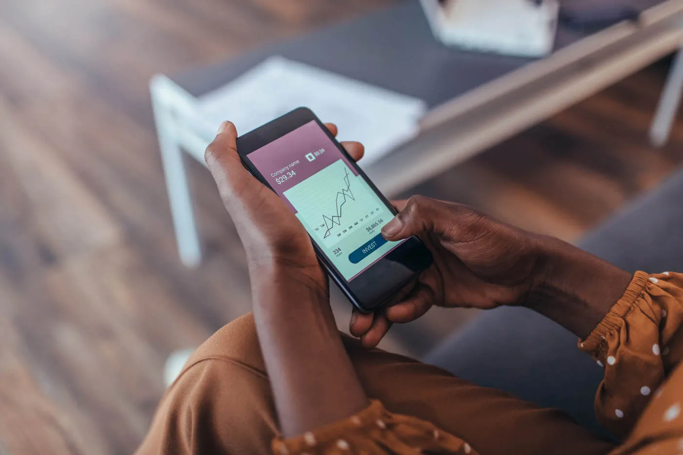 A woman has a stock chart on her phone screen and is about to hit the invest button with her hand.