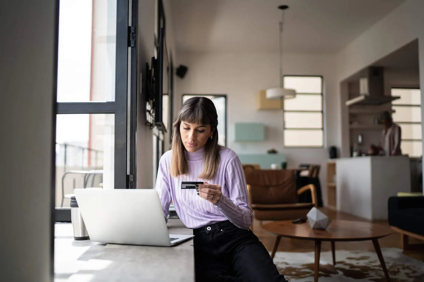 A woman looks at her credit card while using her laptop.