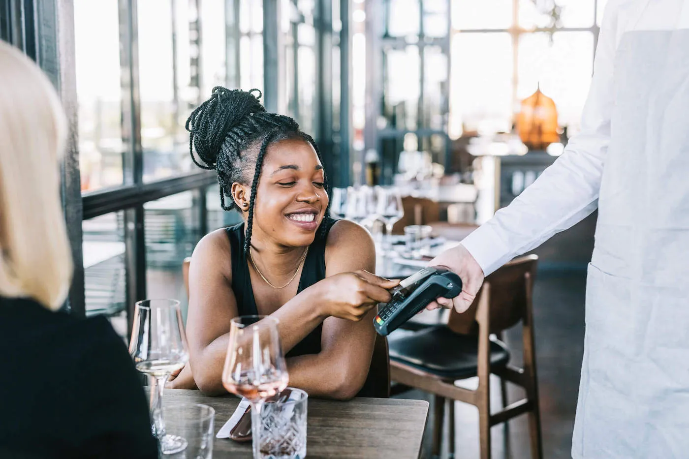 A woman smiles as she pays for her meal at a restaurant by tapping her credit card on the card reader.