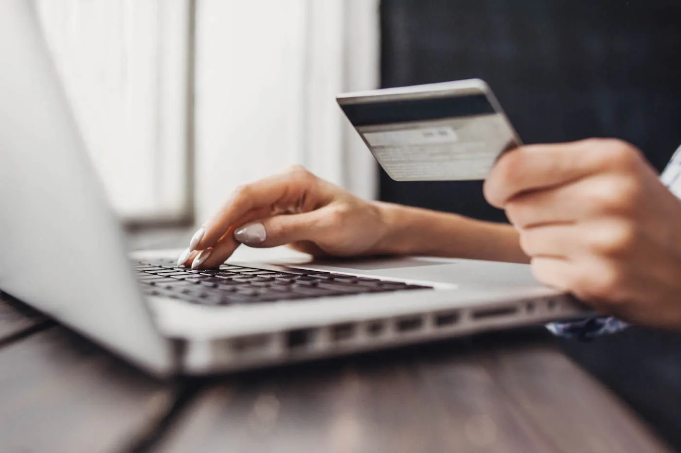 A woman types on her laptop while holding her credit card.