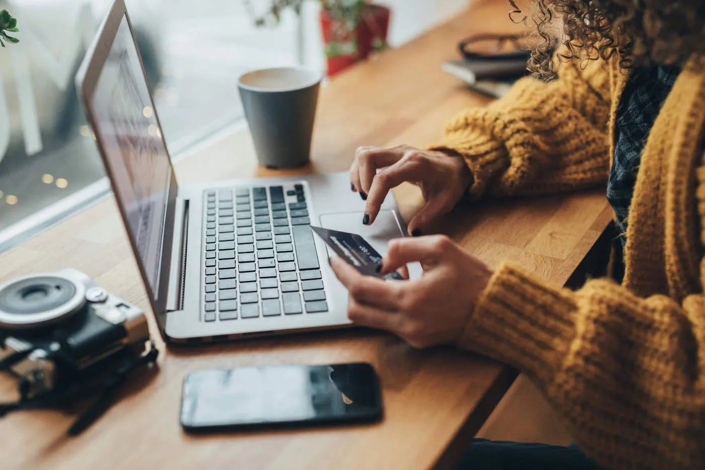 A woman wearing an orange sweater uses her laptop for online shopping while she holds her credit card.