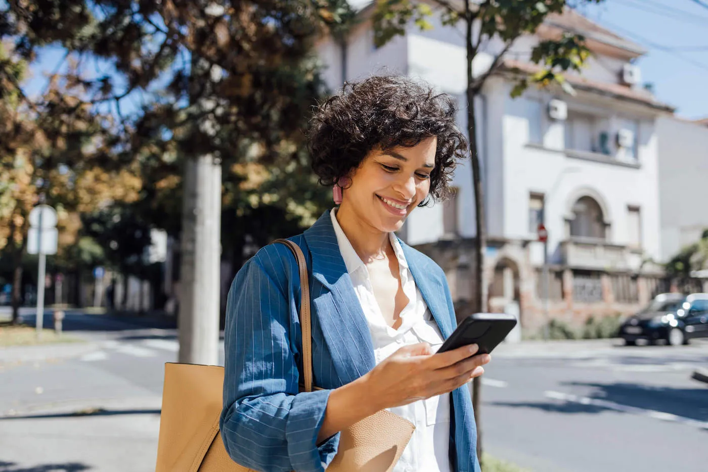 A woman walking outside smiles as she looks at her phone.