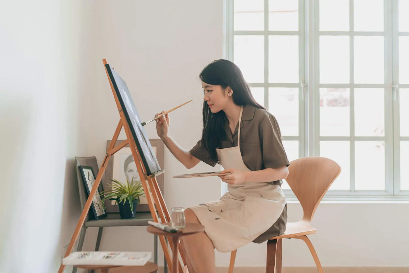 A woman wearing a white apron paints at home.