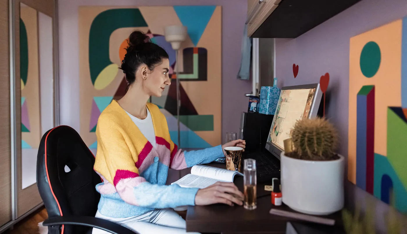 A woman looks at her computer while working from her home office with artwork on her walls.