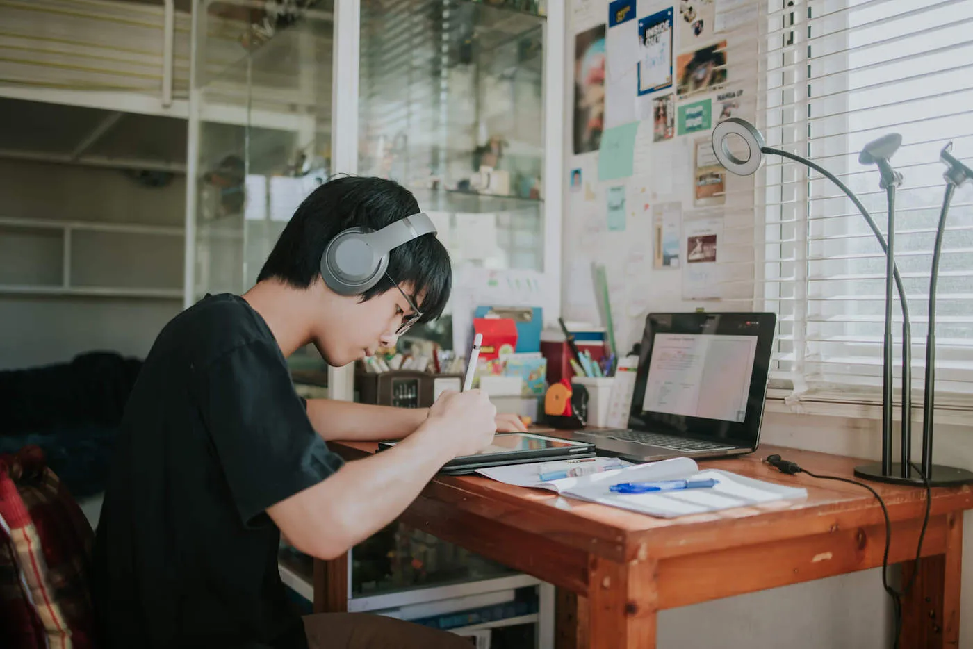 A young boy wearing gray headphones draws on his tablet while at his desk.