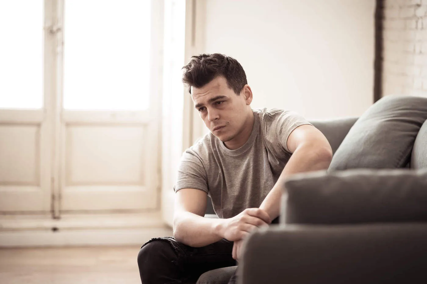 A young man sits on his couch with a sad look on his face.