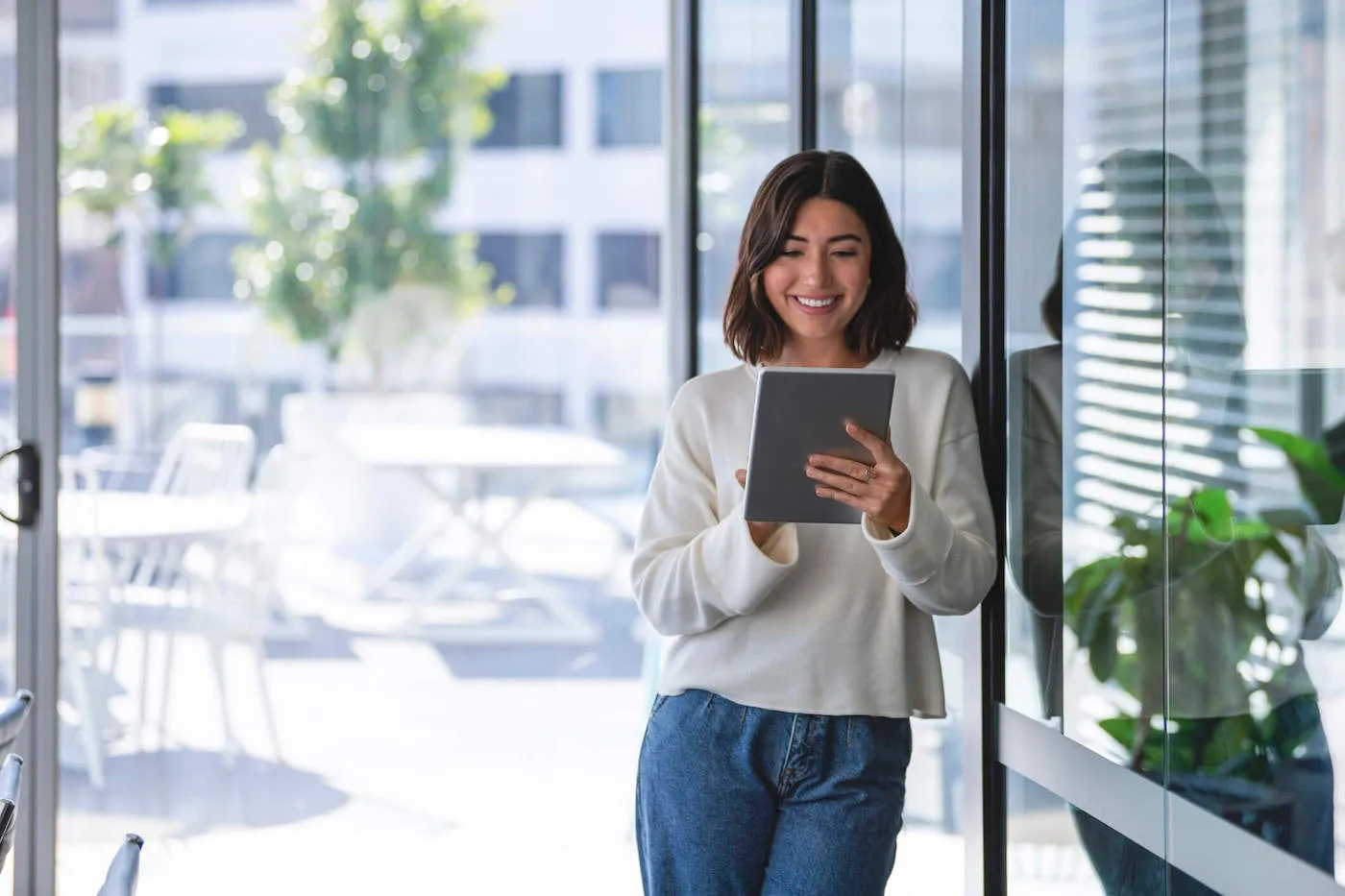 A young woman wearing a white shirt smiles while using a tablet outside.