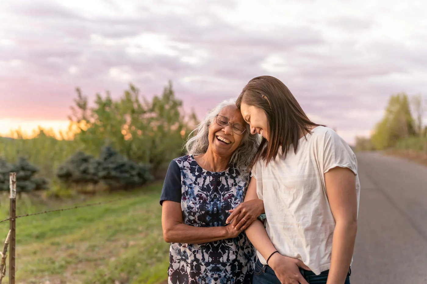 An elderly mother smiles with her adult daughter outside.