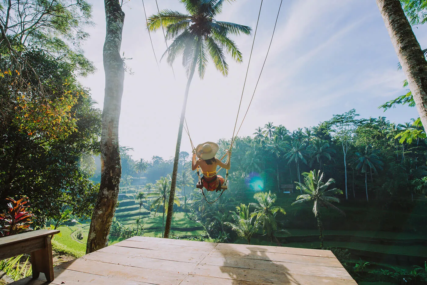 A woman wearing a hat on a large swing in a tropical location.