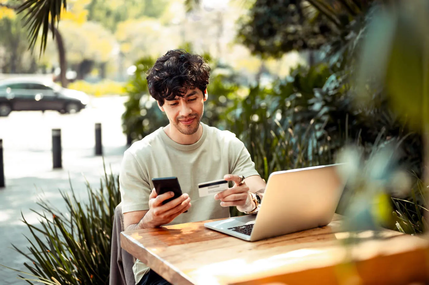 man sitting on a table by an open laptop entering card details on phone