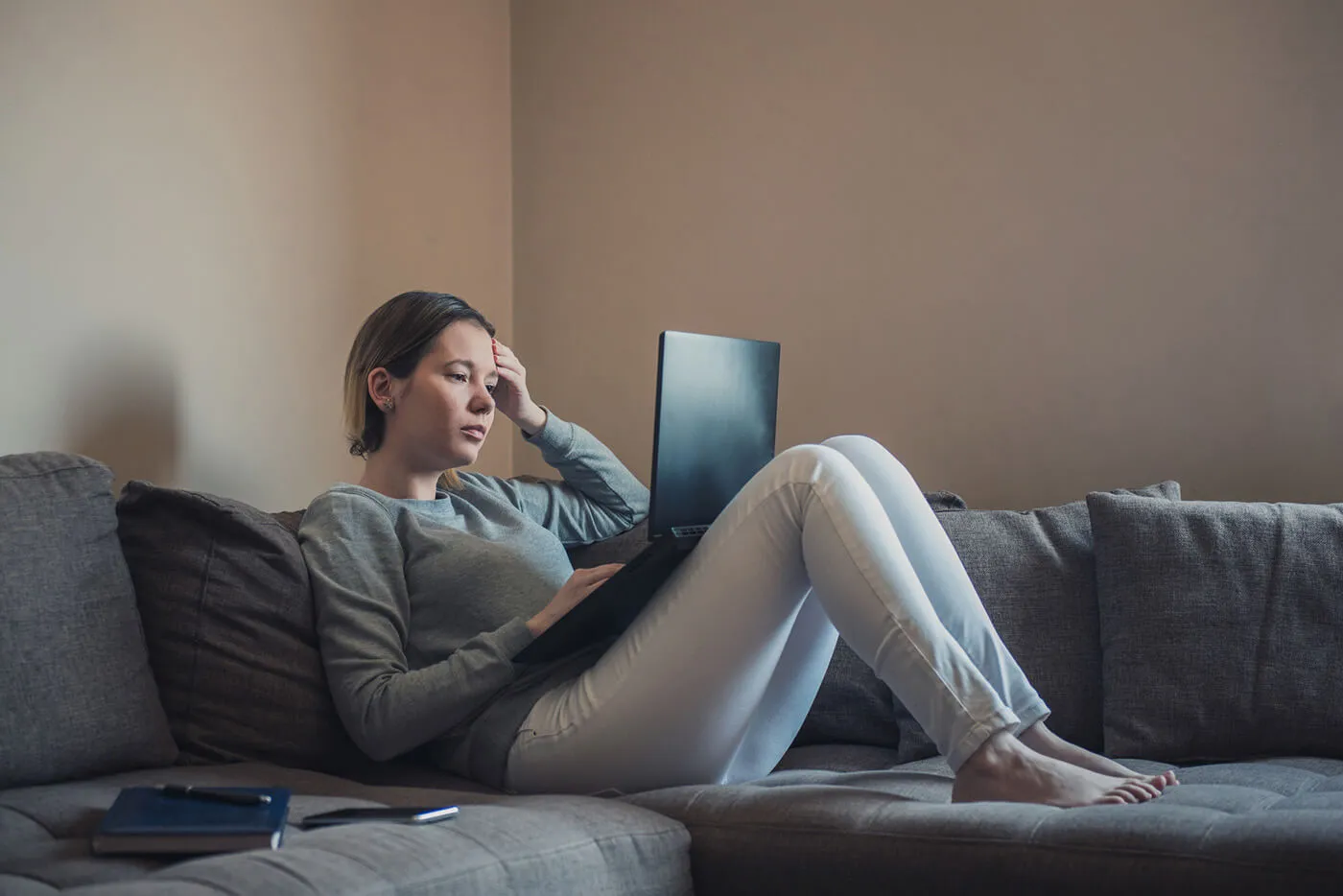 Woman lying down on sofa and using her laptop