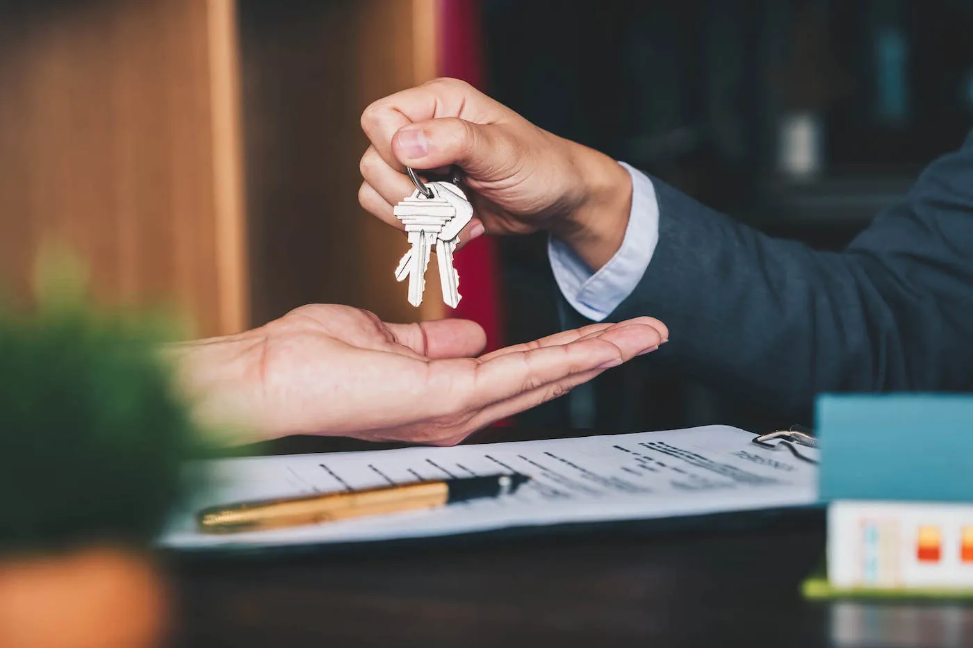 A closeup photo of a person holding keys above a hand with signed documents on the table.