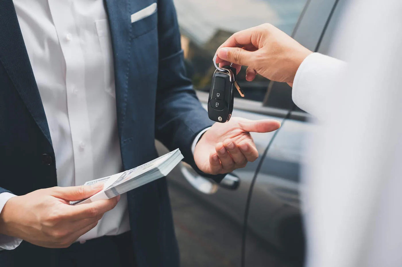 A closeup photo of two people's hands with one person giving car keys and the other person giving a bulk of cash.