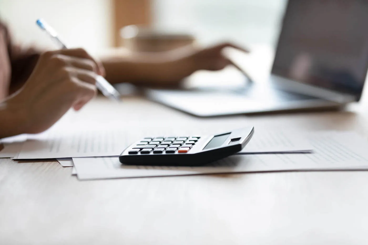 Closeup of female handling brokerage account seated at desk with calculator and laptop.