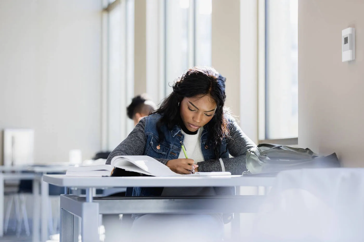 A college students writes on a notebook with her backpack on the table.