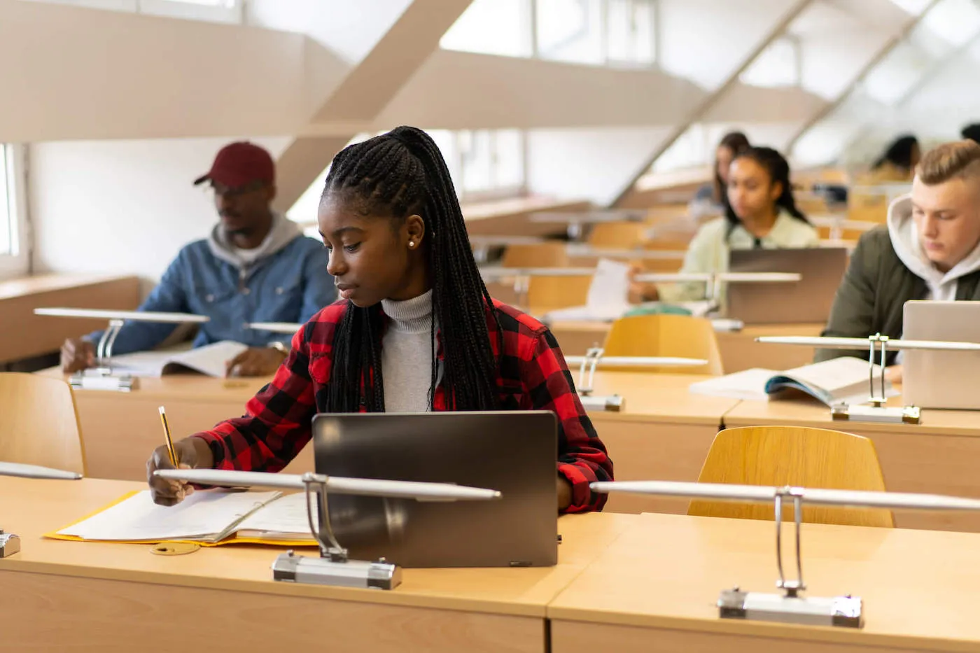 A group of college students are studying in the library with their notebooks and laptops open.