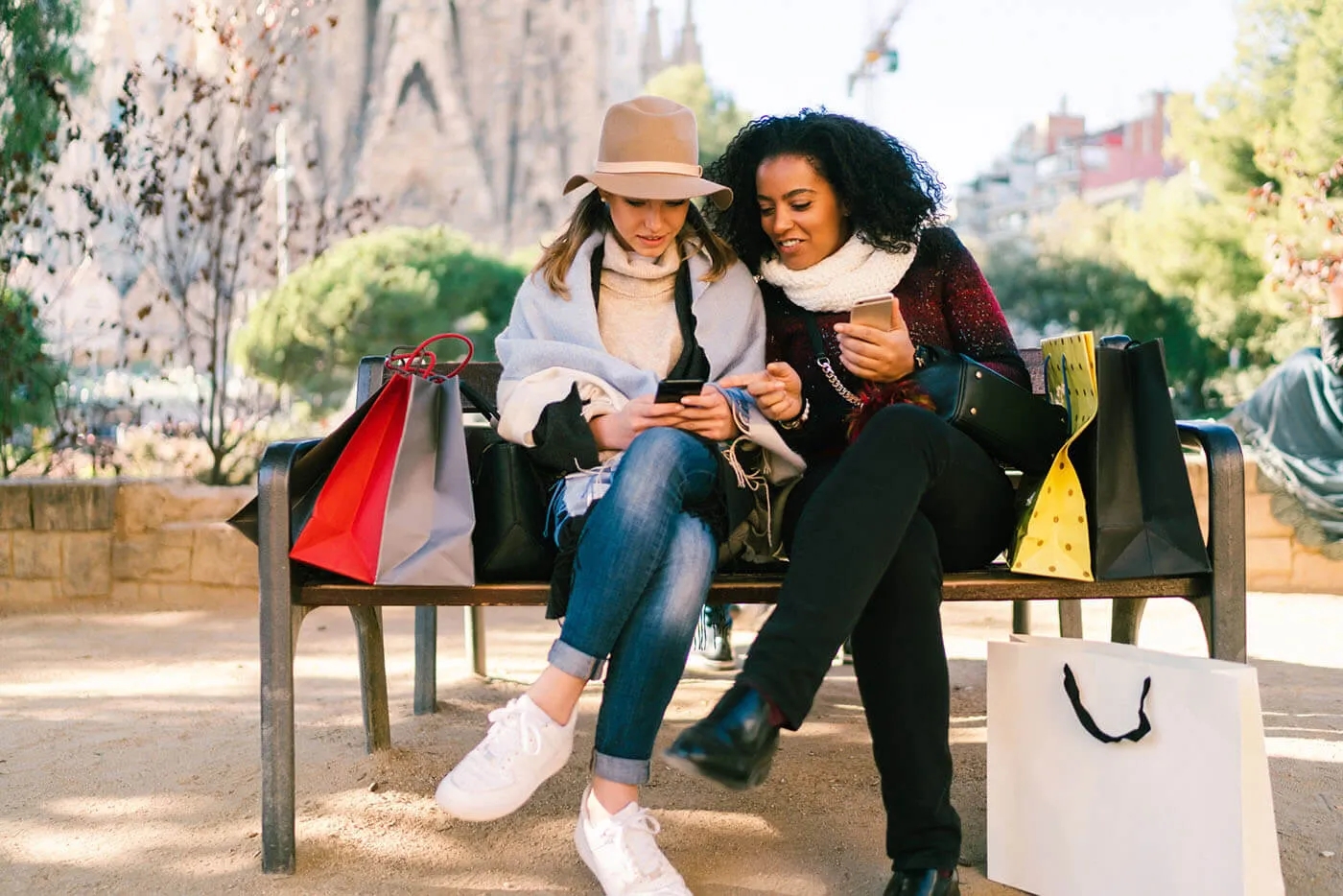 two women sitting on a bench surrounded by shopping bags