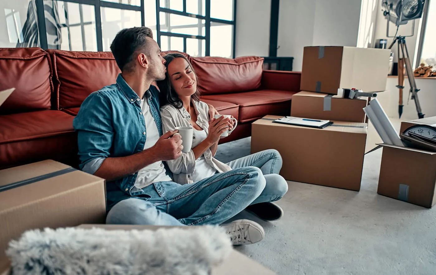 A couple embrace each other while drinking coffee with moving boxes next to them