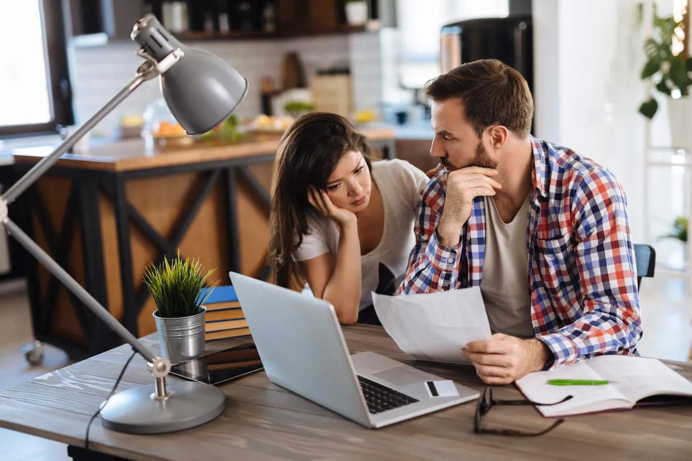 A couple frown together as they look at a document on the office table.