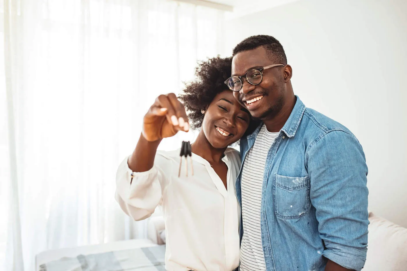 A couple is smiling and hugging each other as the woman holds up the keys to their new home.