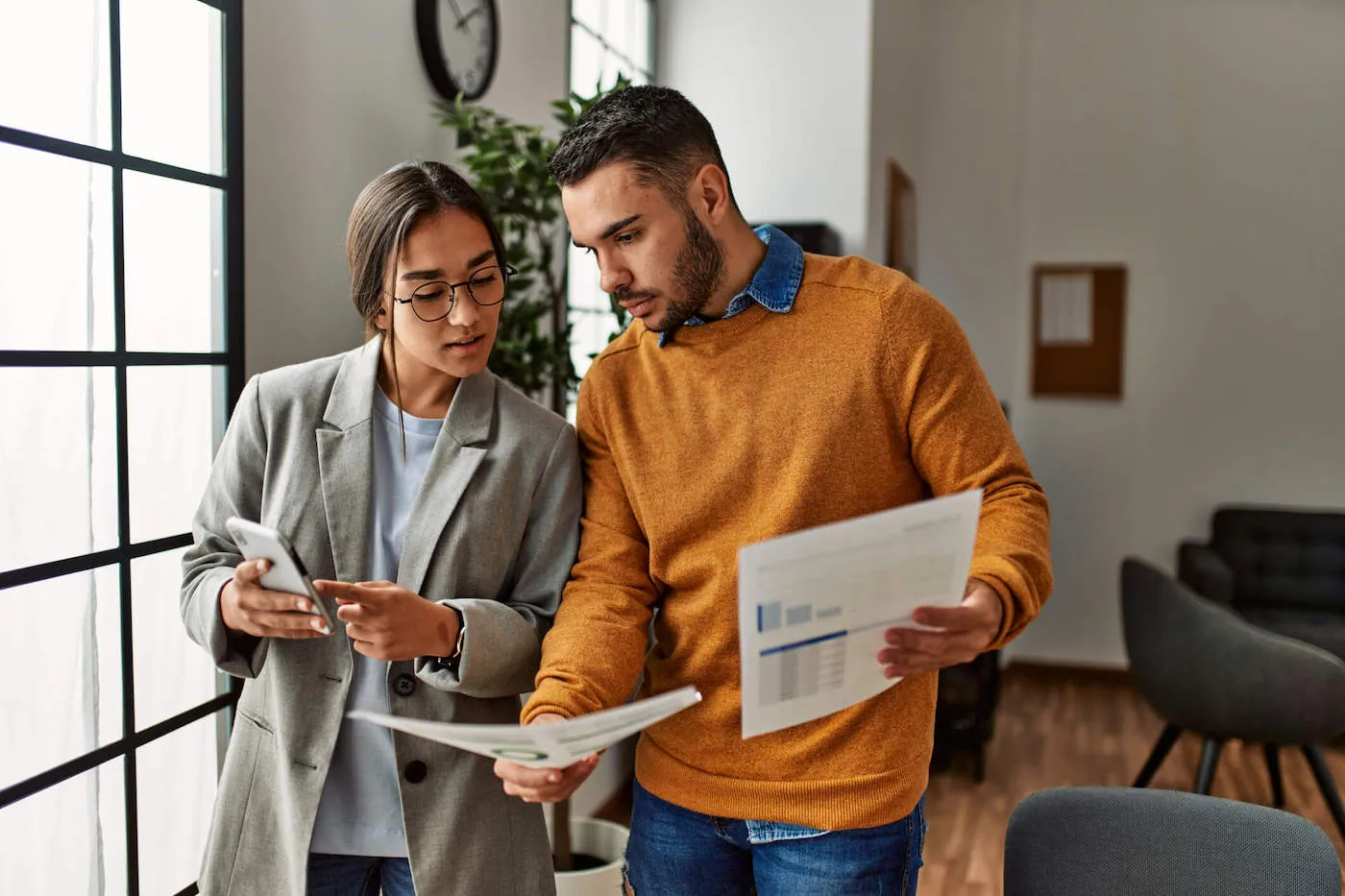 A couple talk with each other while holding documents at home.