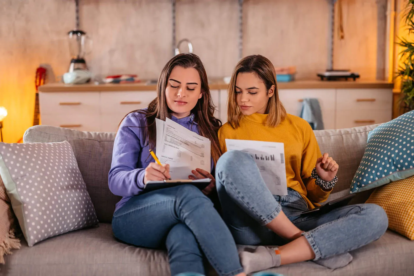 A couple look at documents together while sitting on the couch at home.