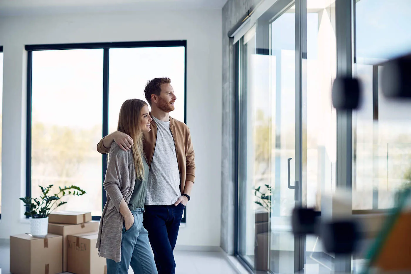 Couple embrace each other while looking out the window of their new apartment.