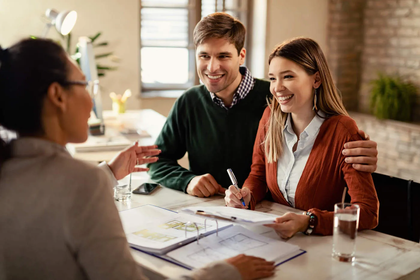 A couple smile at an advisor together as the woman signs a document.