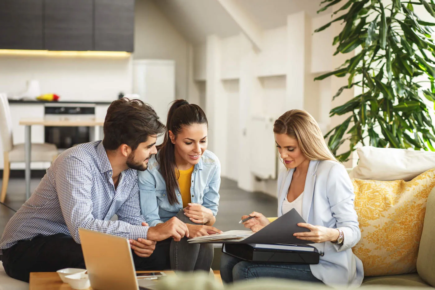 A couple talks with an agent that is showing them a folder with documents while they all sit down.