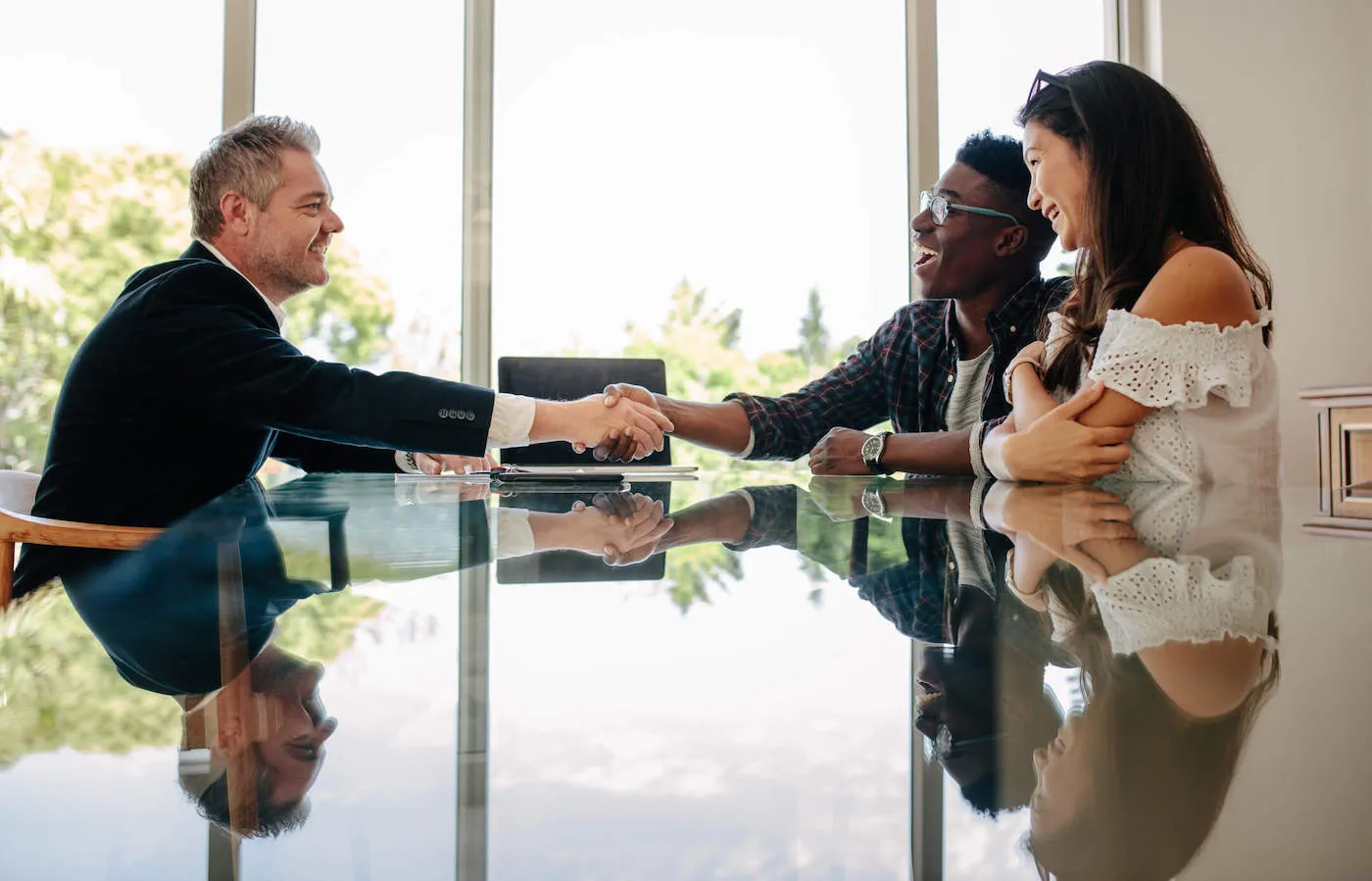 A couple talk with an advisor while the man shakes hands with him from across the table.