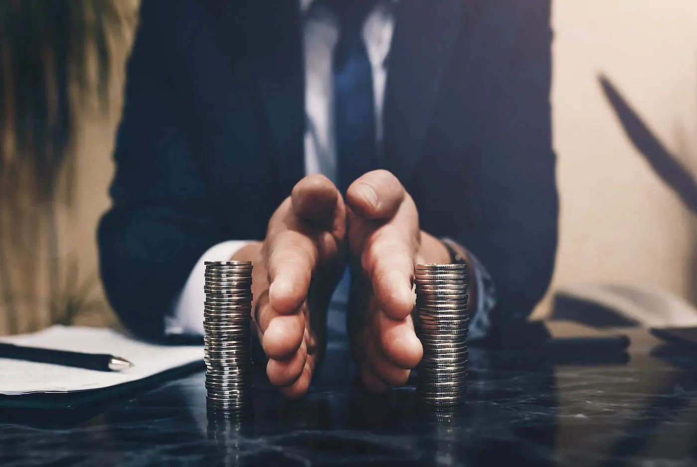 man in suit holding hands separating two coin towers on a table