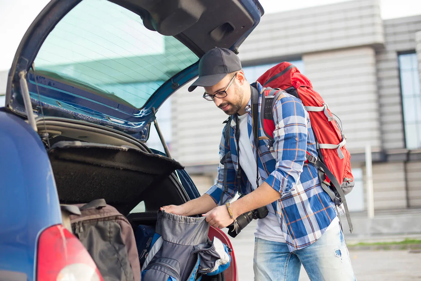 Young man packing backpacks from a car trunk at an airport.