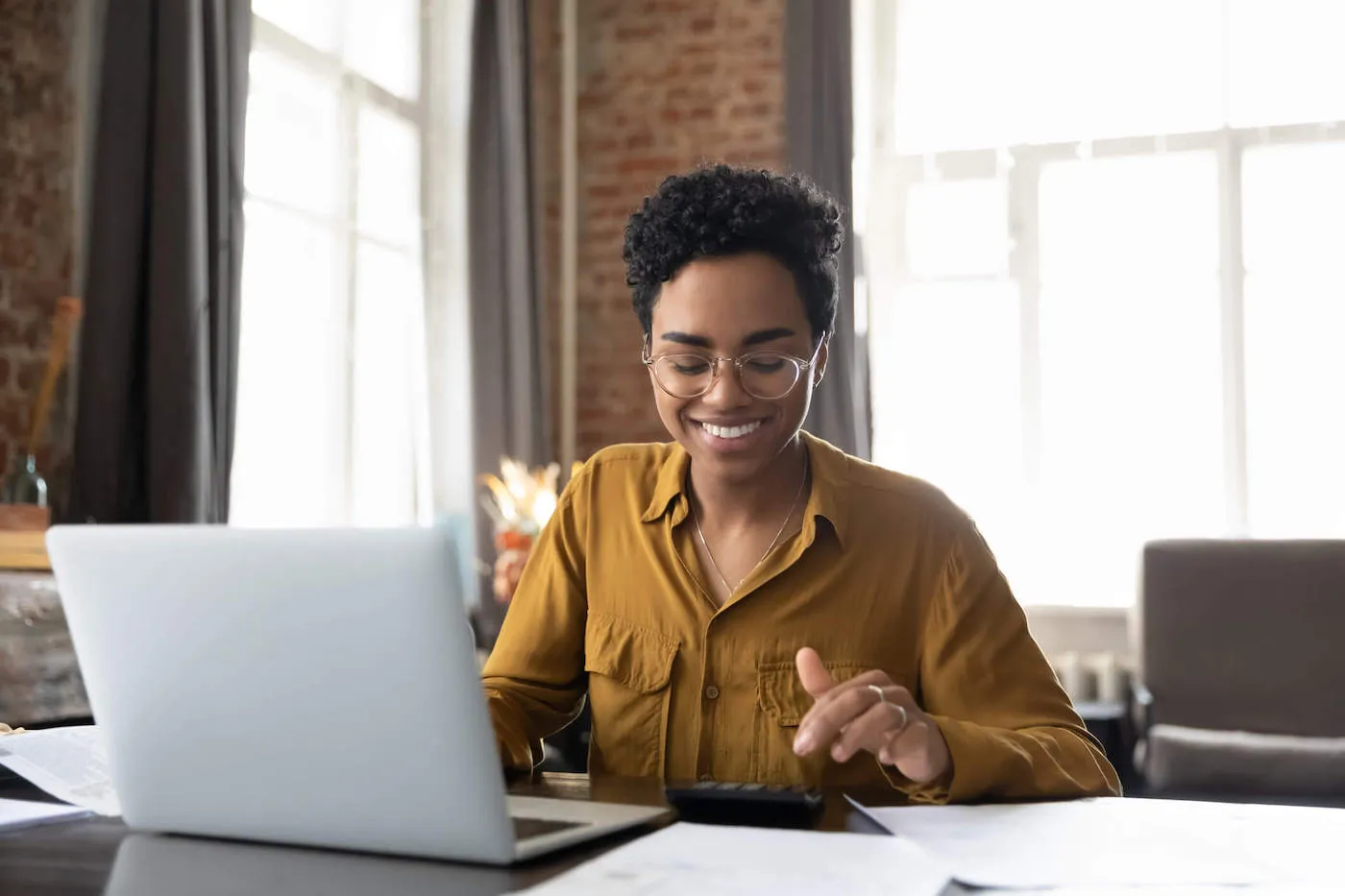 Happy young Afro American entrepreneur woman in glasses paying bills.